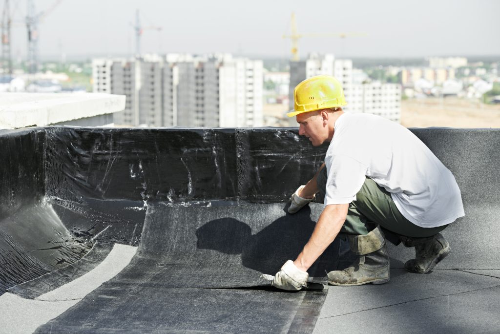 Roofer preparing part of bitumen roofing felt roll for melting by gas heater torch flame