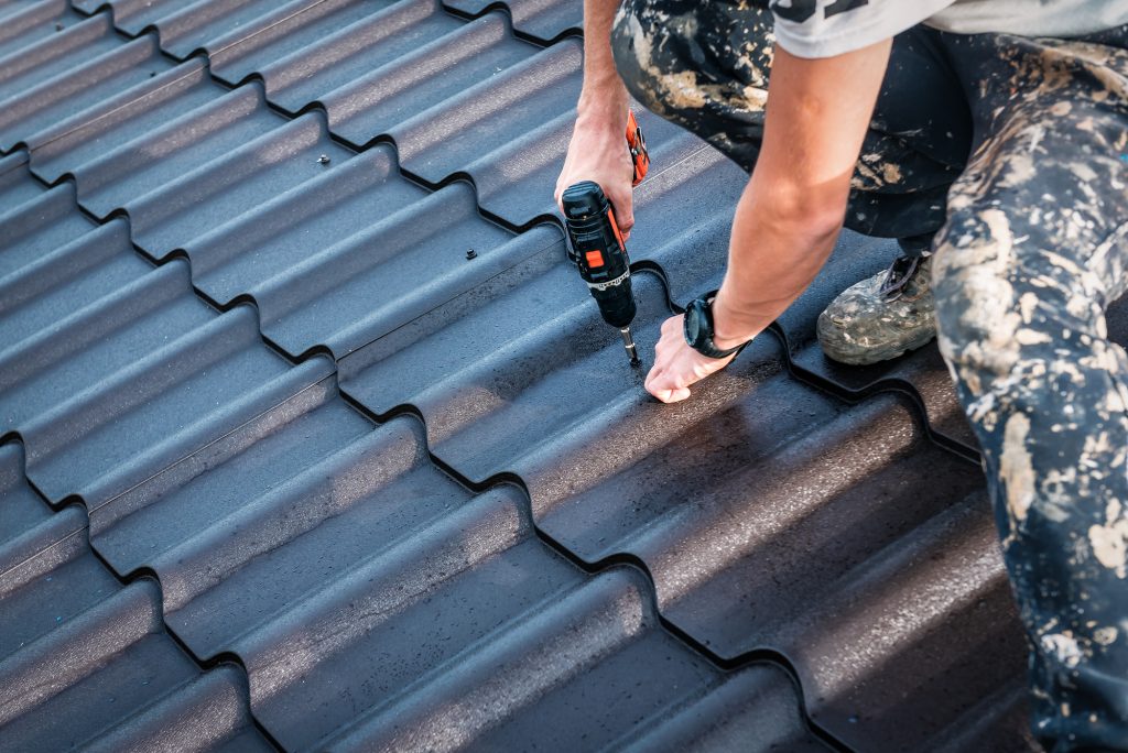 Professional roof worker screws the metal tile