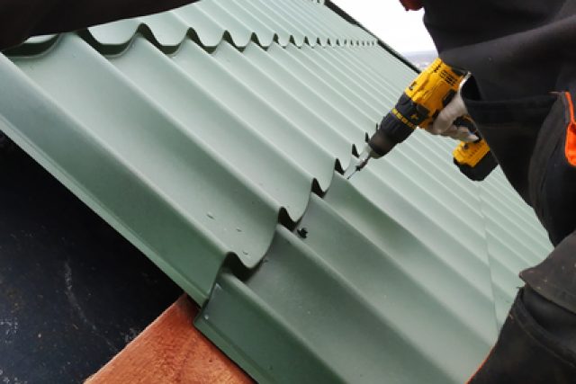 The professional worker works on installation of a roof by sheets of a metal tile